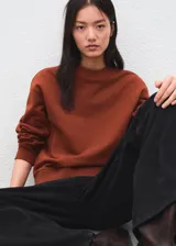 Jersey de punto liso en color marrón terracota, con cuello redondo y diseño de manga larga con puños y bajo de canalé.
