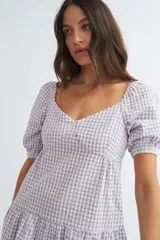 Vestido corto de algodón con estampado de cuadros vichy en color lila y blanco, escote corazón, mangas cortas abullonadas y falda escalonada con volantes.