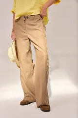Pantalón de lino lavado color beige, de calce recto y diseño relajado. Presenta cintas de lino desflecadas aplicadas en los laterales con pespunte central, pretina con botón metálico, bolsillos delanteros y traseros.