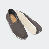 Alpargatas de lona de algodón color crema, estilo slip-on, con elástico en forma de V en el empeine y suela de goma. Presentan la etiqueta de la marca Toms en el lateral.