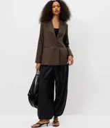 Blazer sastrero de corte alargado con estampado de cuadros pequeños en tonos marrones. Presenta cuello con solapa, cierre frontal con dos botones y mangas largas.