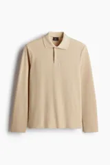 Remera polo de manga larga color beige, confeccionada en tejido acanalado de peso medio. Presenta cuello clásico, tapeta de botones y bajo recto con aberturas laterales.
