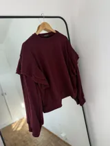 Sweater de punto color bordó con diseño de volados en los hombros y mangas largas. Presenta una textura acanalada fina y corte holgado.