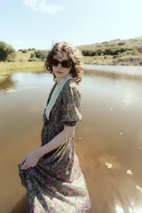 Vestido midi con estampado floral en tonos marrones y azules, cuello en V con detalle de puntilla blanca, mangas cortas abullonadas y cinturón marrón con hebilla dorada.