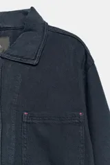 Chaqueta oversize de mezclilla color azul marino, de cuello solapa y manga larga, con bolsillos de parche en el delantero y cierre frontal con botones metálicos.