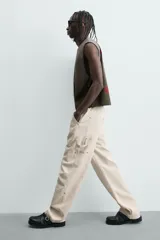 Pantalón relaxed fit color beige, confeccionado en tejido de algodón. Cuenta con bolsillos frontales, bolsillos traseros de plastrón y aplicación de bolsillos plastrón con tira multifunción en la pernera. Cierre frontal con cremallera y botón.