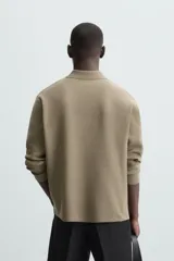 Polo de punto de manga larga con cuello solapa y cierre frontal de botones. Presenta un diseño de corte regular con aberturas laterales en el bajo.