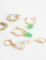 Set de tres pares de aros dorados: un par de aros tipo argolla gruesa, un par de aros con dije colgante de cuentas verdes y un par de aros con dije colgante de perlas y cuentas blancas.