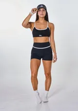 Conjunto deportivo compuesto por un top de breteles finos y un short de tiro alto, ambos en color negro con detalles de ribetes blancos. El top presenta el logo 'bk.' estampado en el frente.