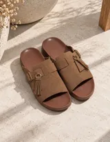 Sandalias de plataforma plana color marrón, con capellada de gamuza sintética, tira con hebilla metálica y detalle de borla colgante.