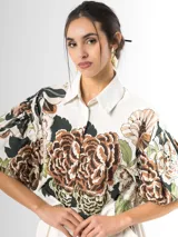 Conjunto de dos piezas confeccionado en viscosa con estampado floral en tonos marrones y verdes sobre base blanca. Incluye una blusa tipo camisa corta con cuello solapa, cierre frontal de botones y mangas abullonadas con diseño globo, y un pantalón tipo culotte de tiro alto, amplio y fluido con pinzas en la cintura.