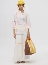 Falda larga blanca confeccionada en broderie de algodón con diseño de paneles escalonados, detalles de galones con transparencias en color azul y naranja, y pretina elástica con cordón ajustable.