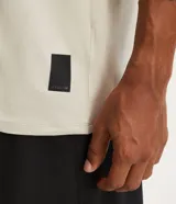 Remera deportiva de hombre con tecnología dry fit, cuello redondo y manga corta. Presenta un diseño liso en color beige con una pequeña etiqueta decorativa en el dobladillo.