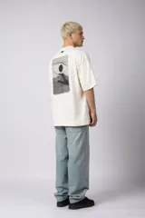 Remera de corte oversize confeccionada en algodón pesado, color negro. Presenta un bordado minimalista en el centro del pecho con forma de ojo y un parche estampado en la espalda que ilustra una mano abriendo una persiana.