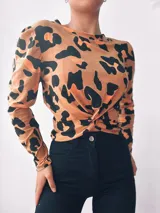 Remera de manga larga color beige con estampado animal print de leopardo en negro. Tiene cuello redondo y un nudo decorativo en la parte delantera.