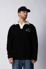 Sweater de punto con textura waffle en color blanco, con cuello polo en contraste color verde oscuro y cierre frontal de botones. Presenta un bordado decorativo en el pecho y un corte relajado.