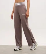 Pantalón deportivo de corte recto color marrón, confeccionado en una mezcla de modal y algodón. Presenta cintura elástica en rib con rayas blancas contrastantes, bolsillos laterales y detalle de lettering bordado en la pierna. Incluye aberturas laterales en el ruedo.