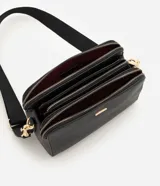 Cartera bandolera Satinato de formato rectangular compacto y textura estructurada, color negro con herrajes dorados. Cuenta con doble compartimento superior con cierre, correa ancha regulable y placa metálica frontal con el logo de la marca.