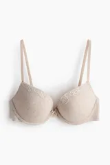 Soutien push-up color beige en punto acanalado, con copas acolchadas, aros, breteles ajustables y cierre de corchetes en la espalda. Presenta detalles de encaje en la parte superior de las copas y un pequeño lazo en el centro.