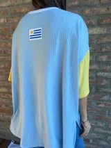 Remera de corte oversize confeccionada en tejido de punto acanalado color celeste, con mangas cortas en color amarillo y detalle de parche bordado con la bandera de Uruguay en la parte superior de la espalda.