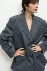 Blazer gris con finas rayas verticales blancas, de corte oversize, solapas de muesca y doble botonadura.