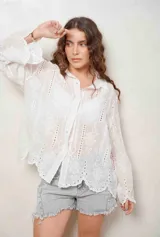 Camisa blanca de manga larga con bordados florales y detalles de ojales, cuello camisero y cierre frontal con botones ocultos.