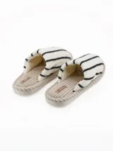Pantuflas abiertas de estilo mule, con capellada de peluche color crema con rayas negras horizontales y plantilla de pana acanalada en tono beige.