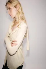 Chaqueta de punto fino color beige, con escote fluido y drapeado, manga larga y cierre frontal cruzado.