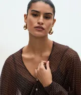 Blusa de poliamida con estampado geométrico, diseño amplio y fluido, escote en V con cierre frontal de botones, mangas largas abullonadas con puños ajustados y acabado con sutil transparencia.