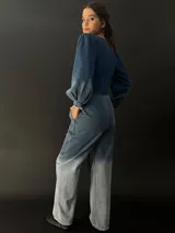 Mono largo de jean azul con lavado artesanal, escote en V regulable con cierre invisible, mangas largas abullonadas y lazo en la cintura.