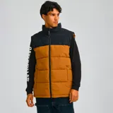 Chaleco acolchado bicolor con diseño de bloques en color marrón y negro. Presenta cierre frontal completo, cuello alto y bolsillos laterales con cierre. Incluye el logo de la marca estampado en el pecho y tecnología resistente al agua y al viento.