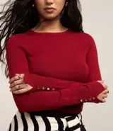 Suéter ajustado de punto color crema, con cuello redondo y mangas largas con botones metálicos en los puños. Confeccionado con viscosa sostenible.