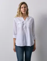 Blusa blanca de lino y rayón, con cuello a la base, escote en V y abertura con botones. Tiene bolsillos en la parte delantera y mangas largas regulables con presilla y botón.