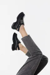 Zueco de cuero negro con plataforma gruesa, punta cuadrada y tira ancha con hebilla metálica y ojales decorativos.