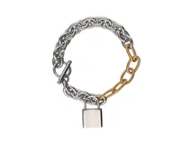Pulsera de eslabones gruesos combinados en acero plateado y dorado, con cierre de barra en forma de T y dije de candado plateado.