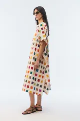 Kaftan amplio de largo midi y escote redondo, con mangas cortas caídas, aberturas laterales y ruedo asimétrico en puntas. Confeccionado en algodón, presenta un estampado de pequeños cuadrados multicolores sobre base blanca.