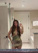 Vestido corto ajustado, color verde claro con estampado de hojas tropicales en tonos tierra. Diseño halter con escote profundo en V y aberturas laterales en la cintura.