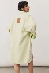 Chaqueta oversize de gabardina color verde claro, con solapa clásica, bolsillos frontales, cierre de botones oscuros y mangas largas con vuelta en tono verde lima vibrante.