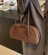 Cartera de mano tipo bowling, confeccionada en gamuza color marrón, con costuras a la vista y manijas largas de cuero al tono.