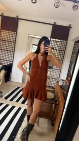 Vestido corto de cuero sintético color marrón, con diseño halter y escote profundo. Presenta un ajuste en el cuello, espalda descubierta y un volado ancho en el ruedo que aporta movimiento.