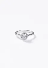 Anillo estilo Lady Di de plata 925 con zirconia central de corte redondo rodeada por un halo de piedras pequeñas y detalles laterales.