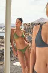 Conjunto de bikini color verde oliva, confeccionado en tela tipo plush. El corpiño es de diseño triangular corredizo con tiras para anudar al cuello y espalda. La bombacha es de corte vedetina con tiras laterales ajustables para anudar.