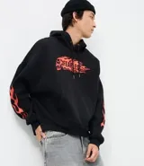 Buzo con capucha negro de corte oversized, con bolsillo canguro y cordones ajustables. Presenta un estampado frontal con una calavera y la palabra 'FEARLESS' envuelta en llamas naranjas y rojas, diseño que se repite en las mangas.