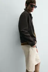 Bermuda de algodón color beige claro, de corte relajado y largo hasta la rodilla. Presenta cierre frontal con cremallera y botón, bolsillos delanteros y bolsillo cerillero, además de bolsillos traseros de plastrón.