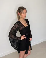Vestido corto de encaje negro con mangas largas acampanadas y lazo ajustable en la cintura.