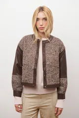 Chaqueta bomber color bordó con mangas de cuero sintético marrón y cuerpo de tweed con patrón de espiga. Cierre frontal con botones a presión y cuello redondo.