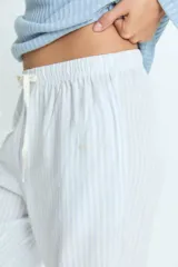 Pijama compuesto por una remera de manga larga en color celeste con textura acanalada y cierre frontal con botones, y un pantalón largo de corte recto en color blanco con rayas verticales celestes y cintura elástica con cordón ajustable.
