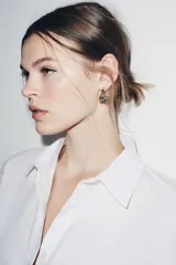 Pendientes tipo aro abierto doble, de metal dorado, con incrustaciones de piedras brillantes de diferentes tamaños y tonos oscuros en uno de los aros.