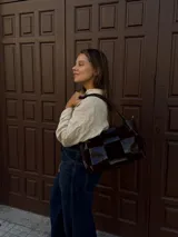 Cartera de hombro confeccionada en cuero y gamuza con diseño de damero, combinando paneles de texturas lisas y aterciopeladas. Presenta una manija trenzada y detalles de costuras artesanales en los laterales.