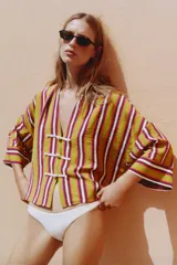 Camisa de rayas multicolor con predominio de verde, cuello redondo con escote en V y mangas anchas. Cuenta con cierre frontal mediante alamares de cordón blanco.